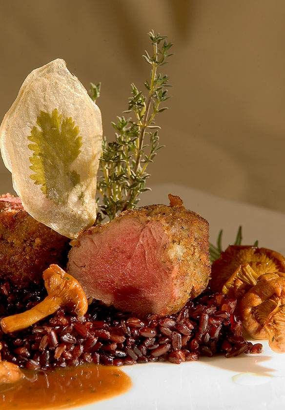 Plat gastronomique composé de viande tranchée, de riz noir, de sauce et de garniture, servi sur une assiette blanche.