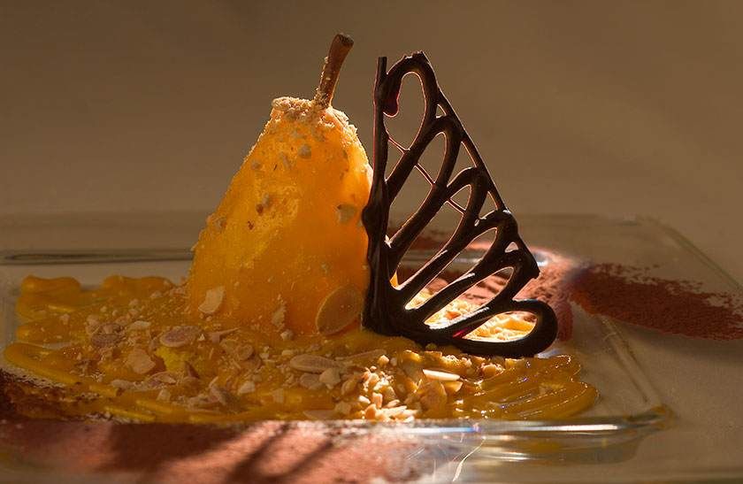Dessert avec poire caramélisée et décoration papillon en chocolat sur une assiette en verre