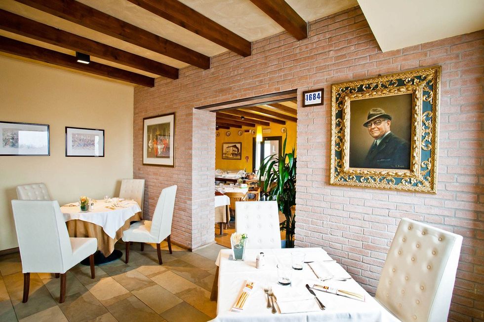Elegant restaurant interior with white tablecloths, brick walls, wooden beams, and framed artwork.