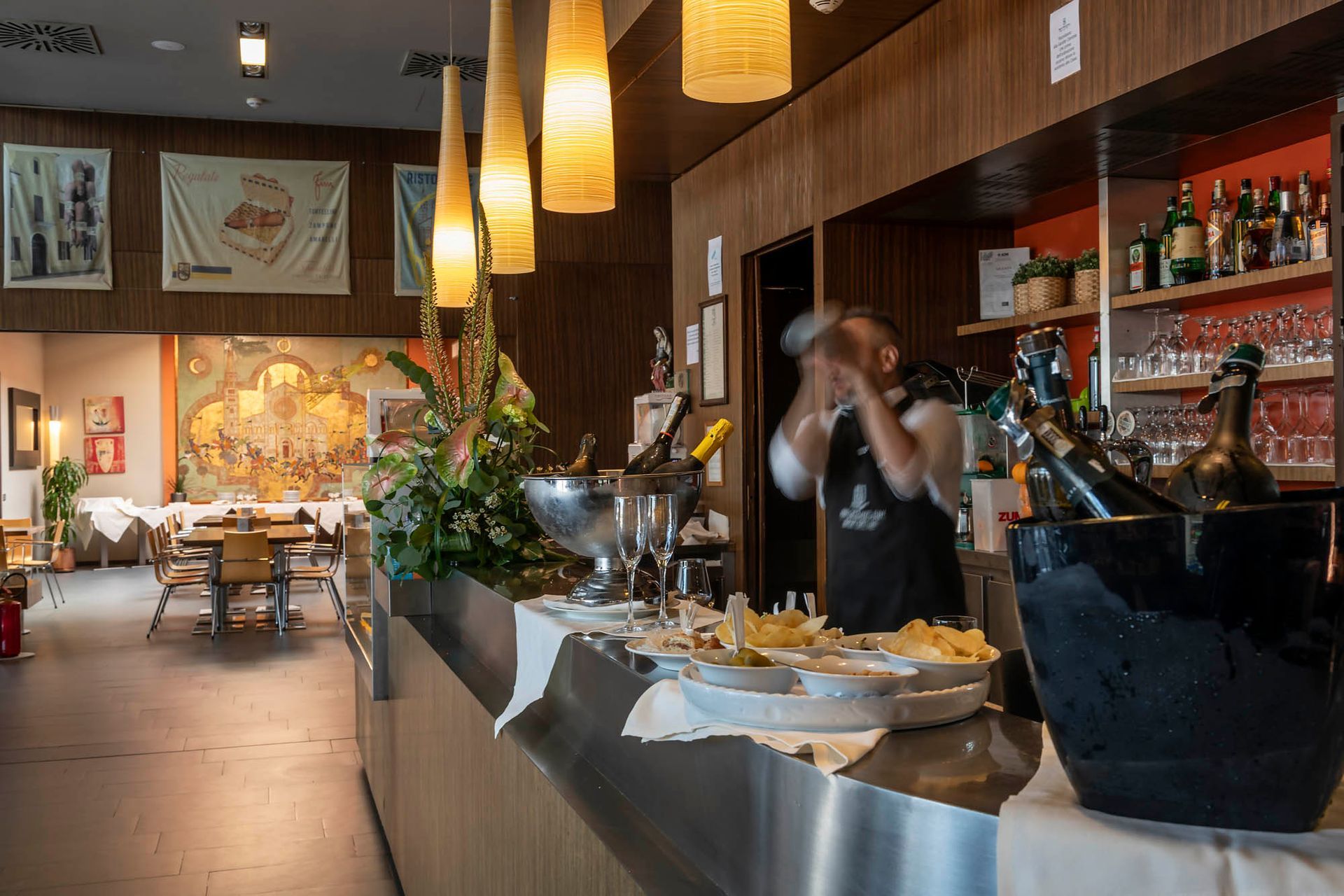 Elegant restaurant interior with a bartender behind the counter and hanging pendant lights.