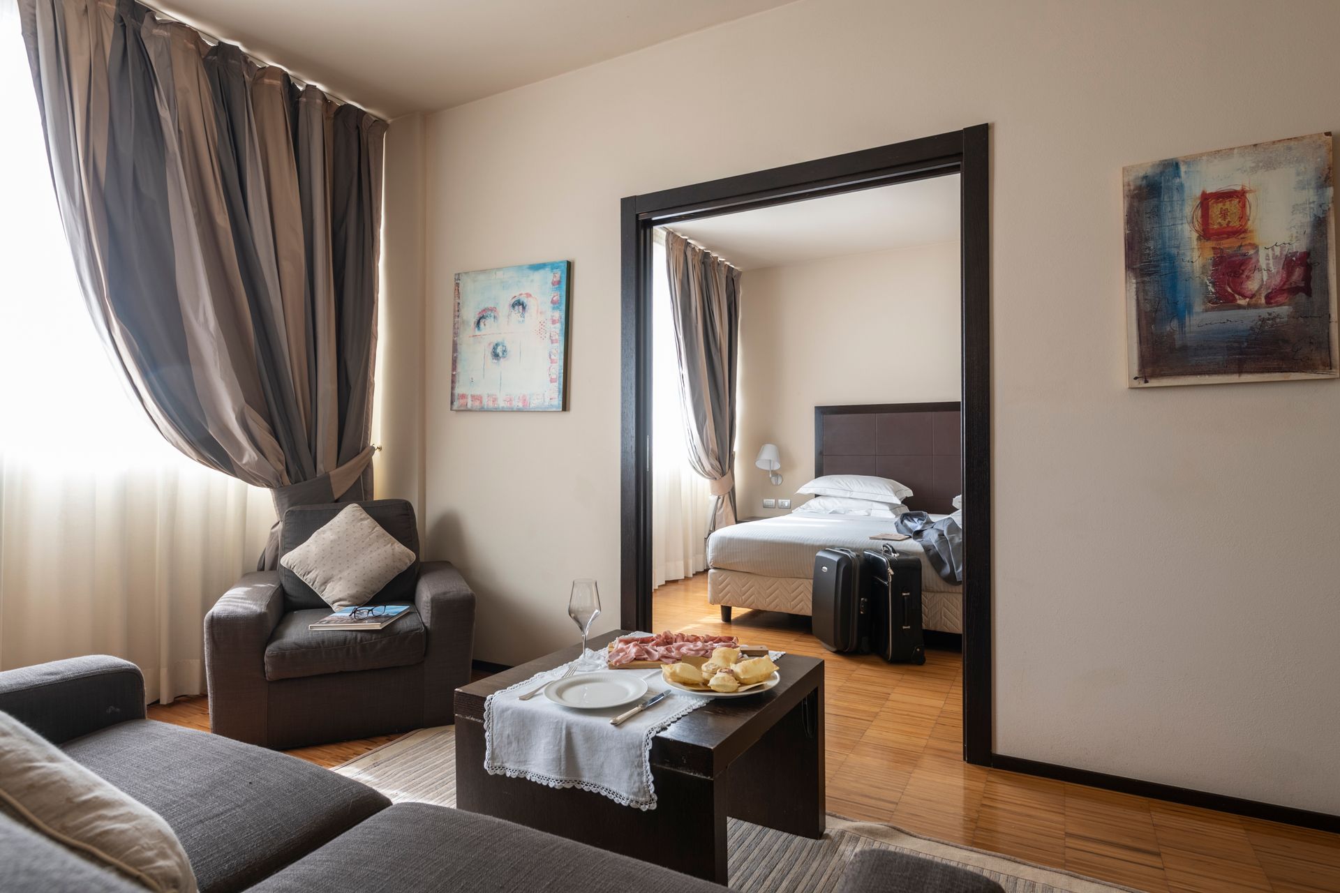 Cozy living room with sofa, armchair, coffee table, and doorway to a bedroom with a bed.