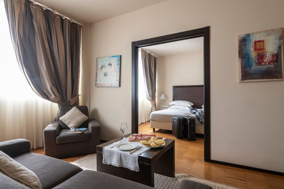 Cozy living room with sofa, armchair, coffee table, and doorway to a bedroom with a bed.