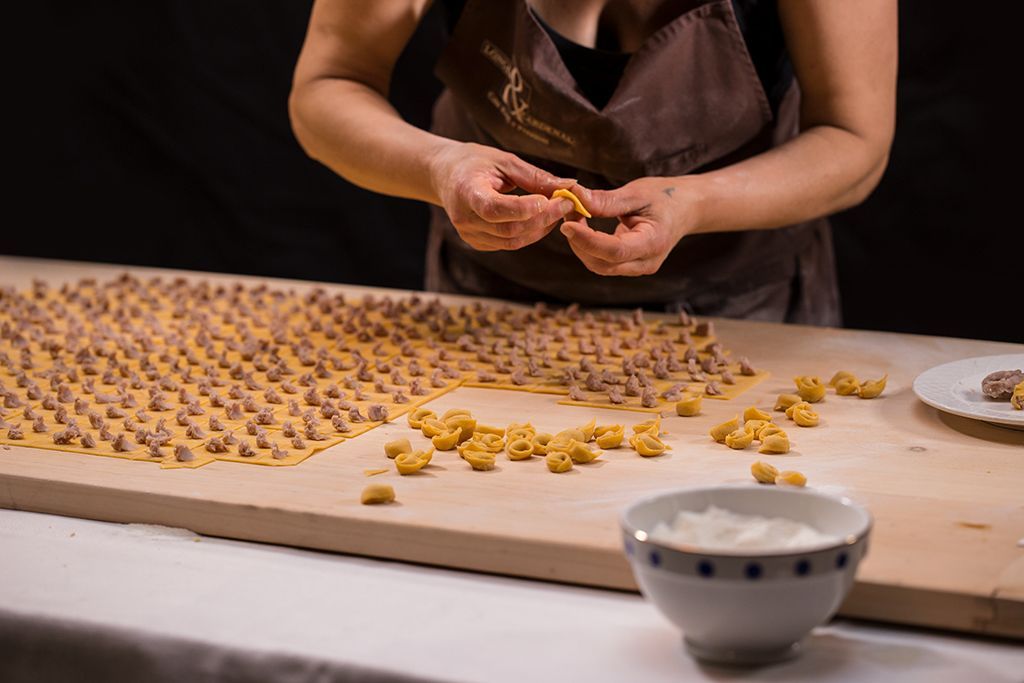 Person shaping small pasta pieces on a wooden board, with a bowl nearby