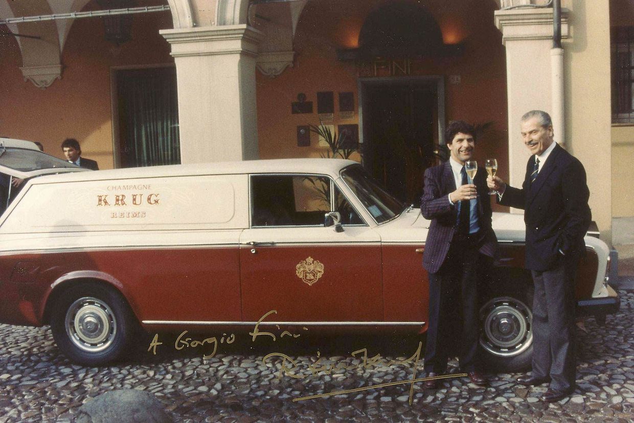 Two people standing beside a red and cream vintage station wagon outside a building