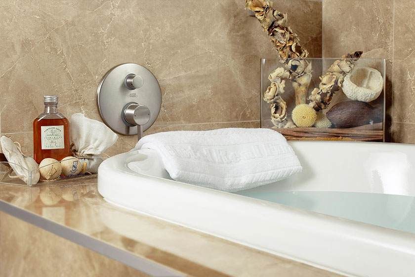 Salle de bains luxueuse avec baignoire blanche, serviette pliée, bougies et galets décoratifs sur le rebord.