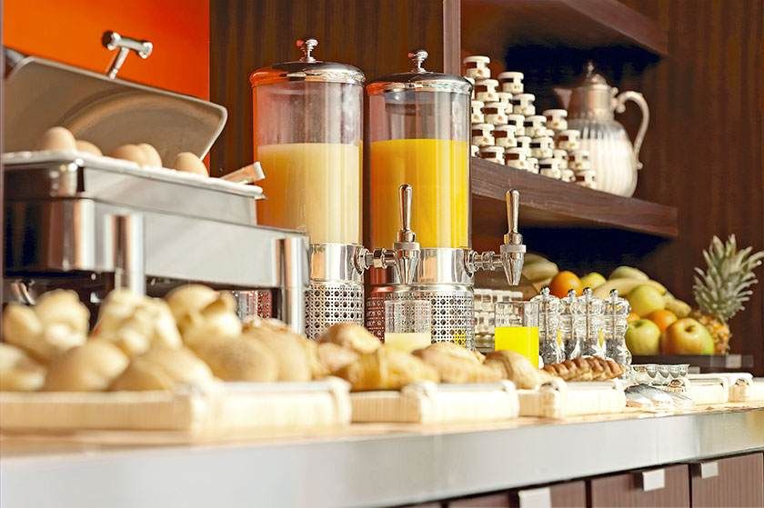 Buffet de petit-déjeuner avec distributeurs de jus, viennoiseries, fruits et bocaux disposés sur un comptoir