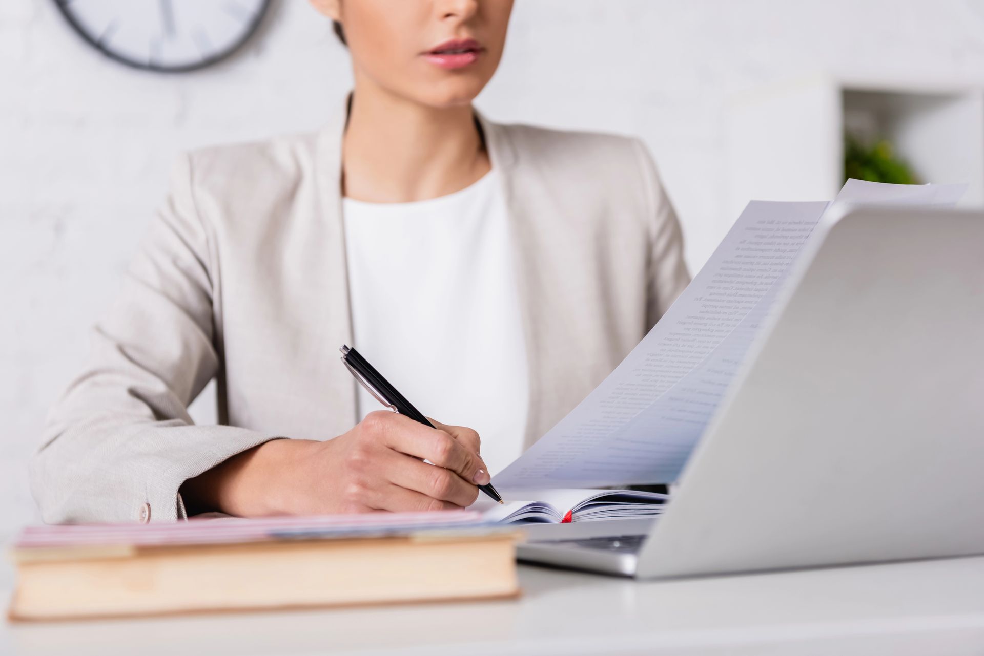 Una mujer está sentada en un escritorio con una computadora portátil y escribiendo en una hoja de papel.