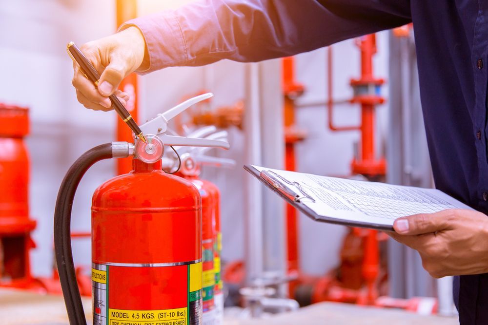 Technician Inspecting a Red Fire Extinguisher With a Clipboard — Pasiv Fire in Wollongong, NSW