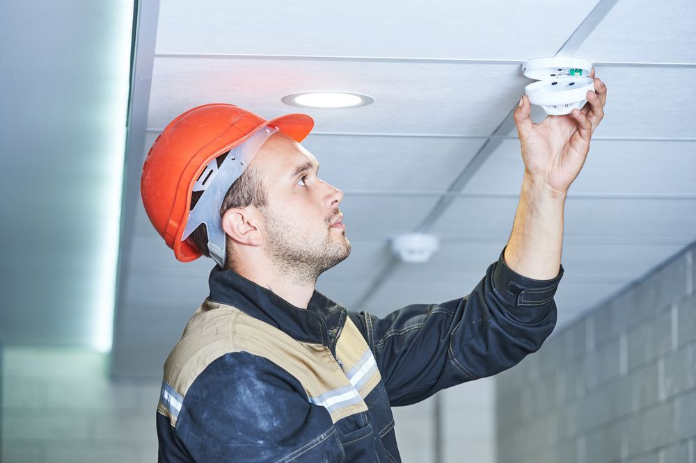 Worker Installing Smoke Detector On The Ceiling — Fire Protection in Merimbula, NSW