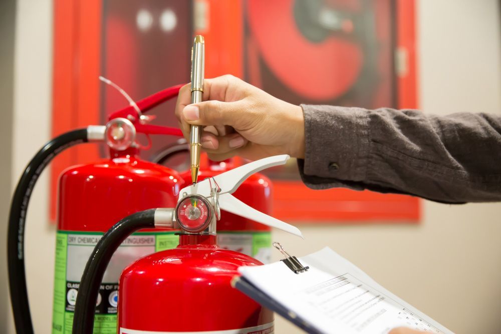 Hand Checking a Red Fire Extinguisher in Front of Other Extinguishers — Pasiv Fire in Wollongong, NSW