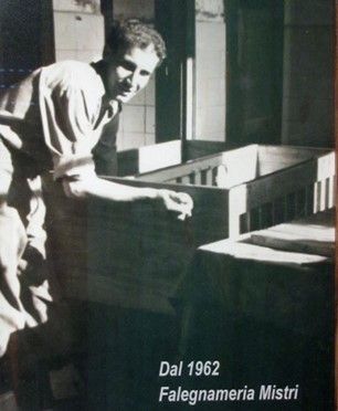 Foto in bianco e nero di un uomo chino su una grande macchina o un modello in legno in un'officina.