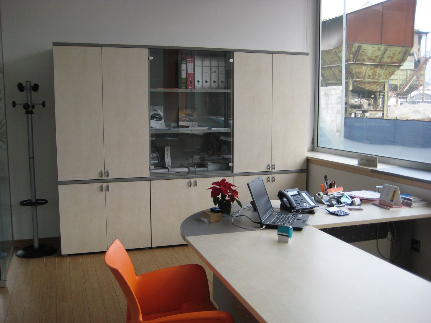 Ufficio con armadietti, scrivania, sedia arancione e un'ampia finestra con vista sull'esterno.