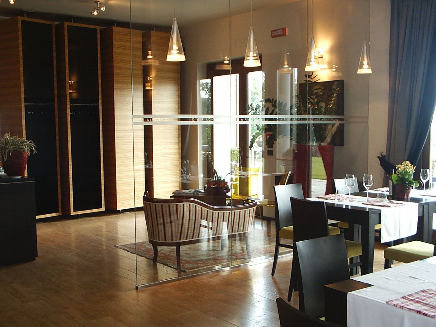 Sala da pranzo moderna del ristorante con tavoli, lampade a sospensione e ampie finestre che lasciano entrare una calda luce naturale.