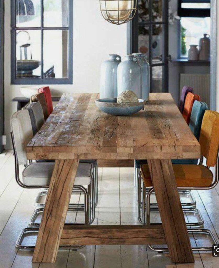 Un rustico tavolo da pranzo in legno con sedie colorate e spaiate in una luminosa stanza moderna.