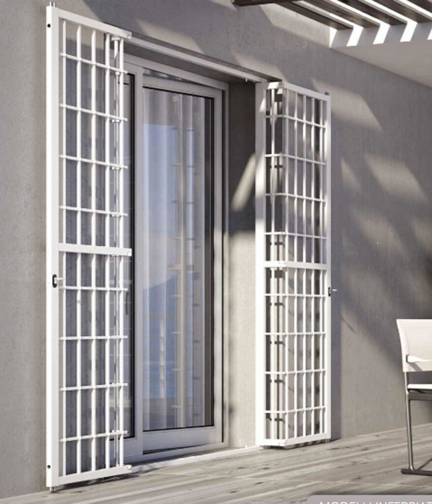 Cancelli di sicurezza in metallo bianco che fiancheggiano una porta-finestra in vetro su una parete esterna grigia.