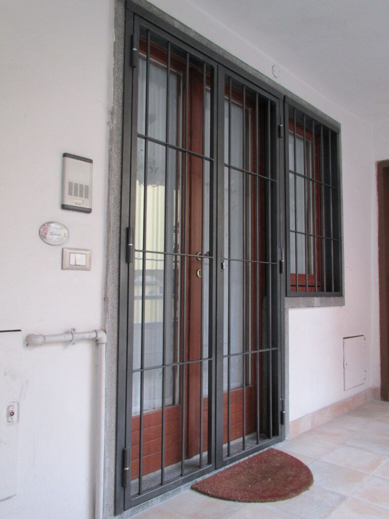 Ingresso principale con porta a vetri con sbarre, piccola finestra e zerbino su un portico piastrellato.