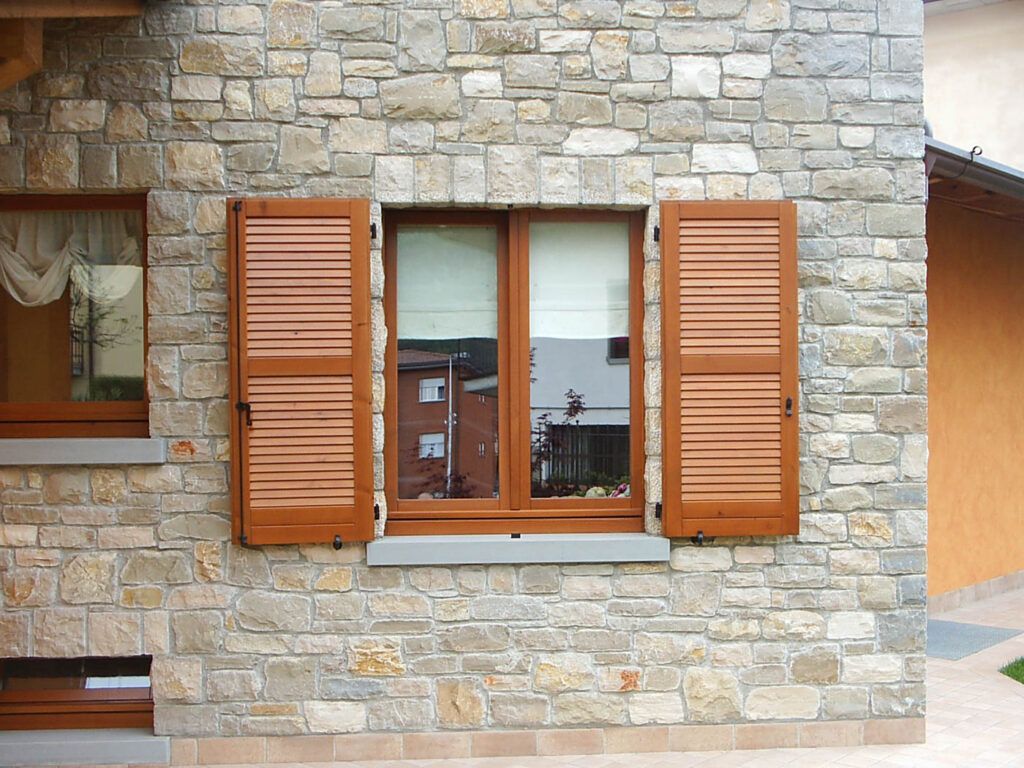 Muro di pietra della casa con una finestra incorniciata da persiane di legno marrone