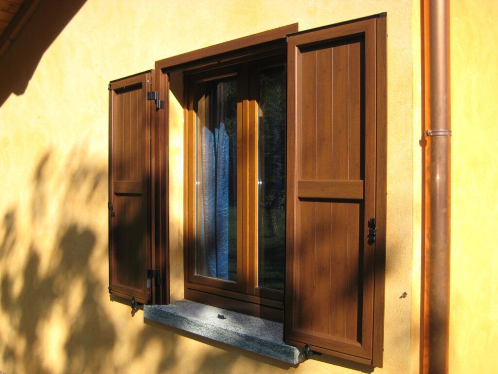 Finestra in legno con persiane aperte su una parete gialla illuminata dal sole