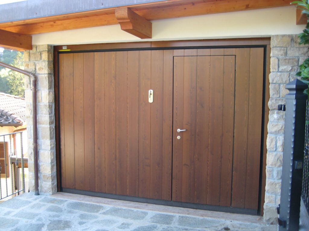 Porta da garage doppia in legno incastonata in un muro di pietra sotto una tettoia in legno.