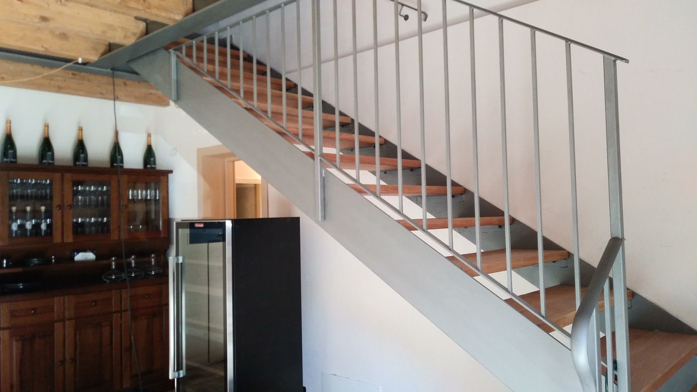 Scala interna con ringhiera bianca accanto a un mobile in legno scuro e un frigorifero in una stanza moderna