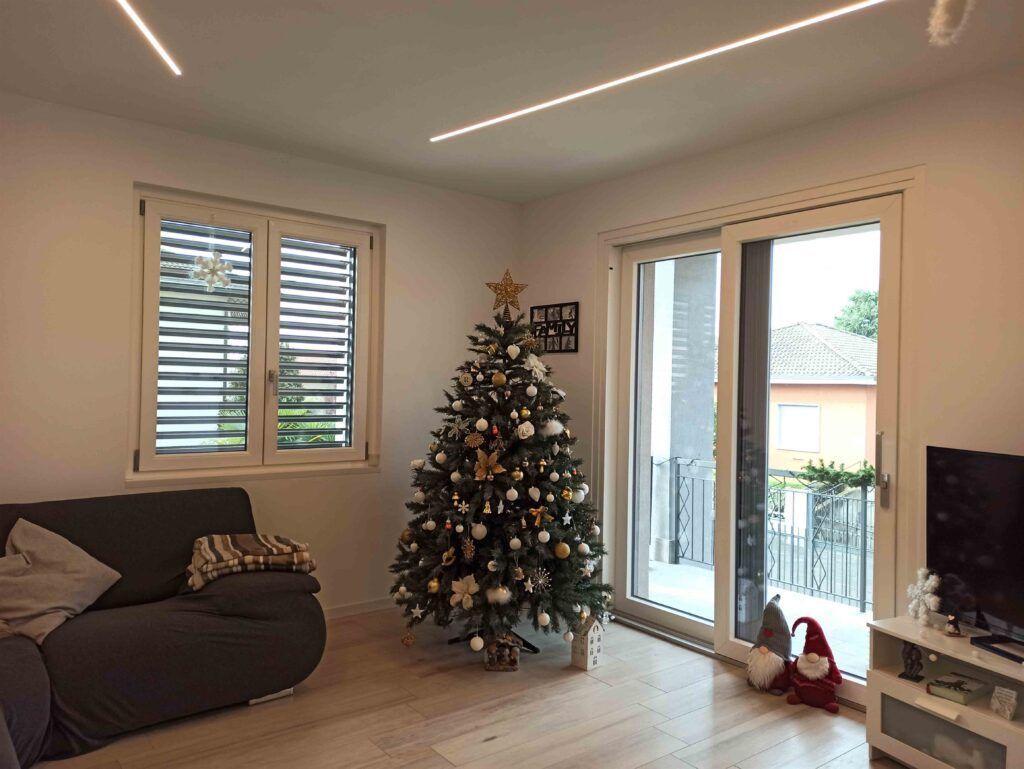 Soggiorno con albero di Natale decorato, divano e porta scorrevole in vetro che si apre su un balcone.