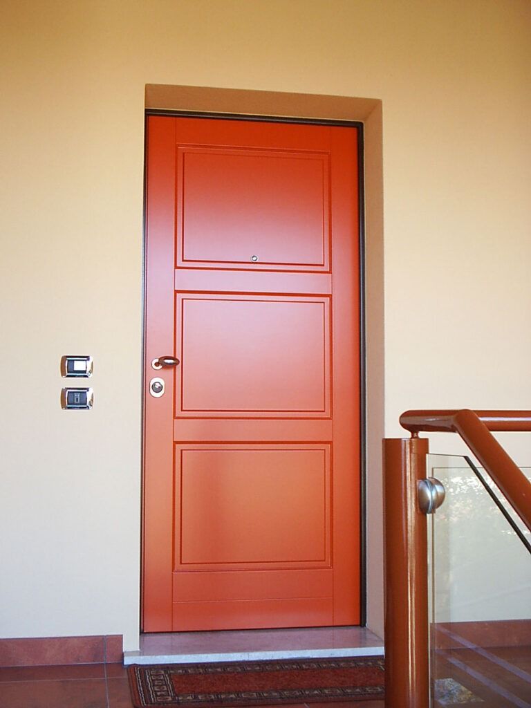 Una porta arancione in un corridoio beige accanto a una ringhiera delle scale e a degli interruttori a parete.