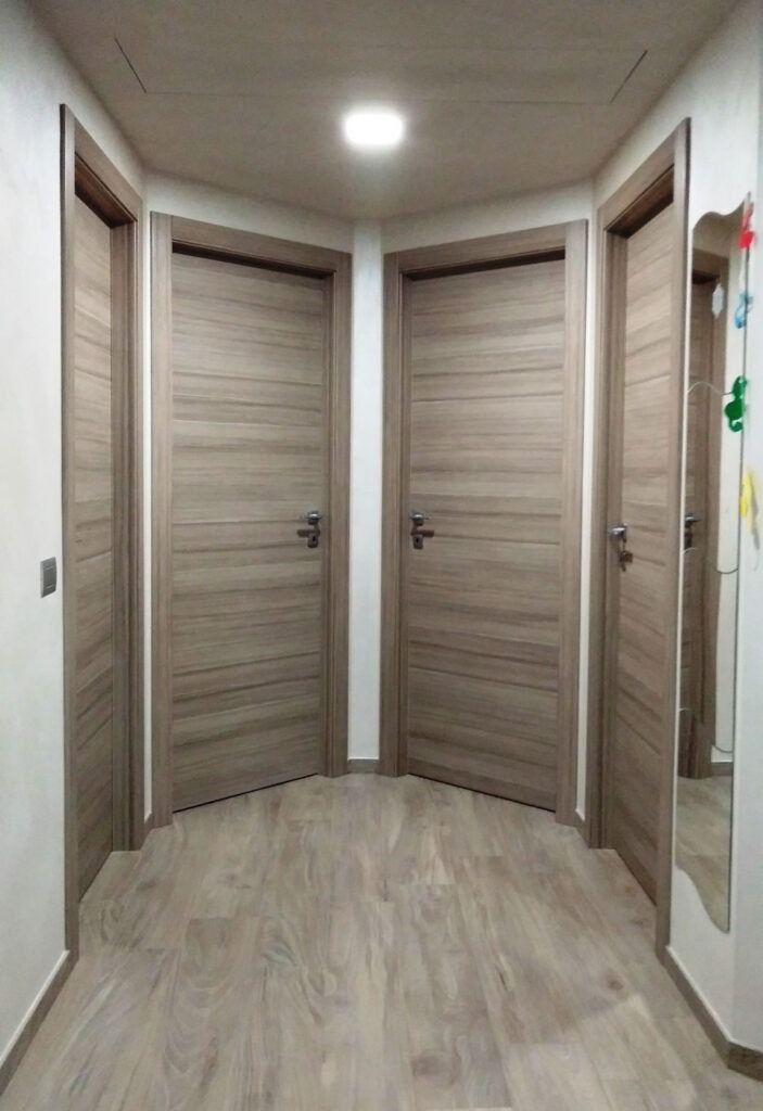 Corridoio curvo con tre porte in legno chiaro e uno specchio sulla parete di destra.