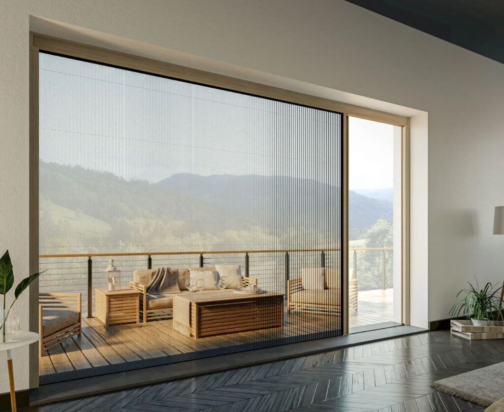 Soggiorno moderno con ampia finestra che si apre su un balcone con vista sulle montagne e zona salotto esterna.