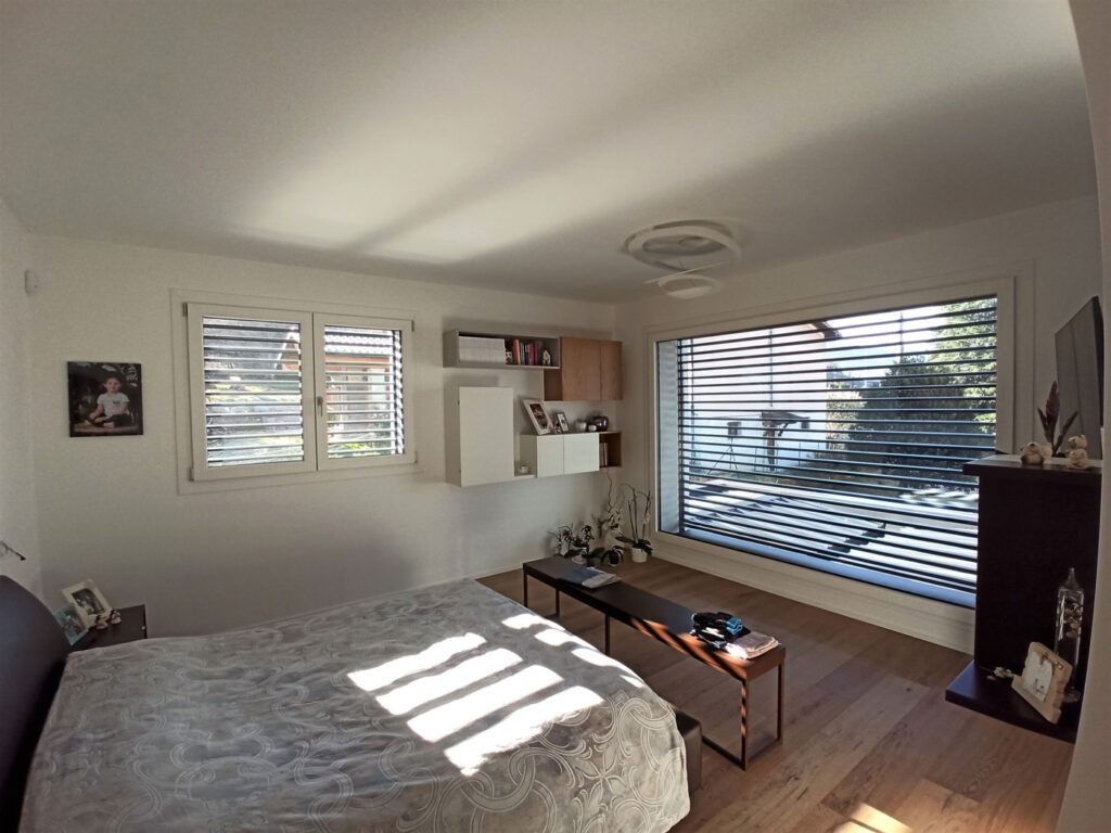 Camera da letto luminosa con letto, grandi tende alle finestre, luce del sole sul pavimento e un tavolino da caffè.