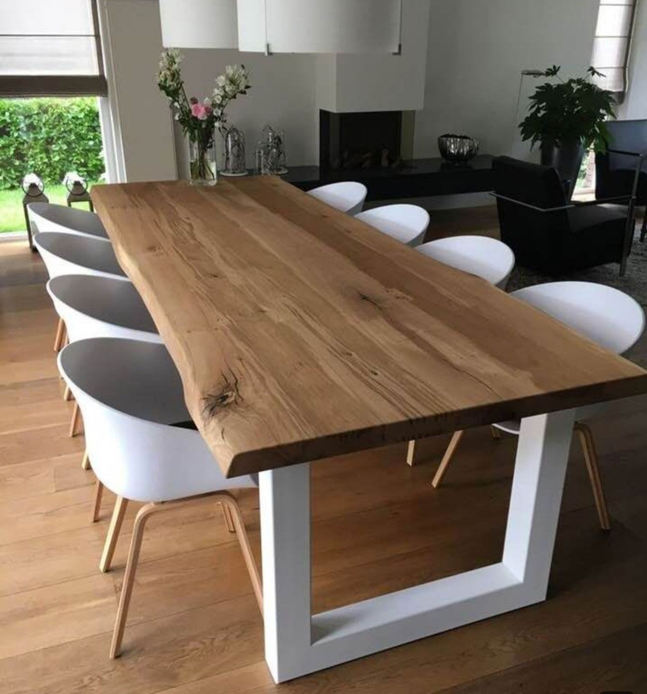Sala da pranzo moderna con un lungo tavolo di legno, sedie bianche e ampie finestre che si affacciano sul verde.