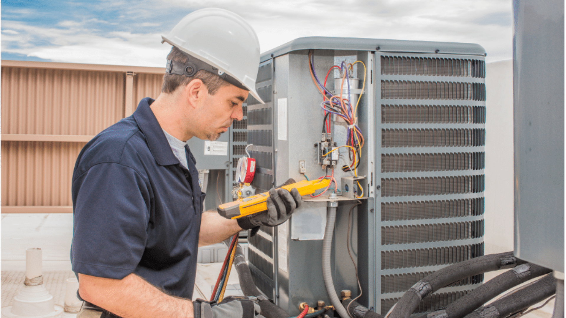 Technician testing rooftop HVAC unit with a multimeter beside a large metal air conditioner.