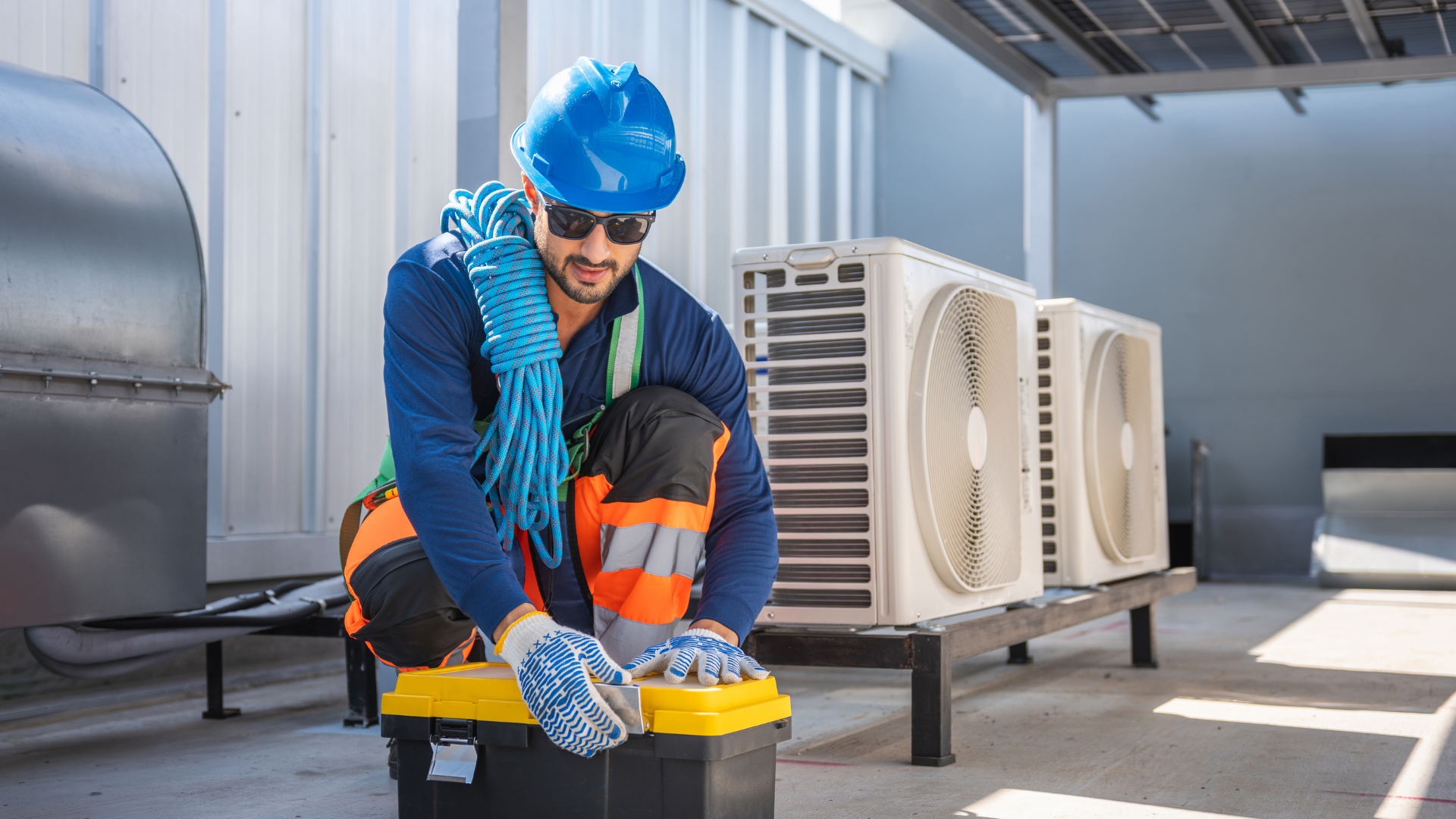 Worker on a rooftop using a crane to lift a large HVAC unit into place.
