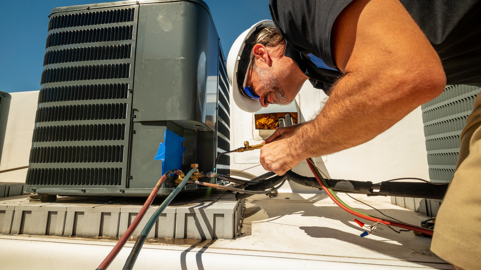 Worker on a rooftop using a crane to lift a large HVAC unit into place.