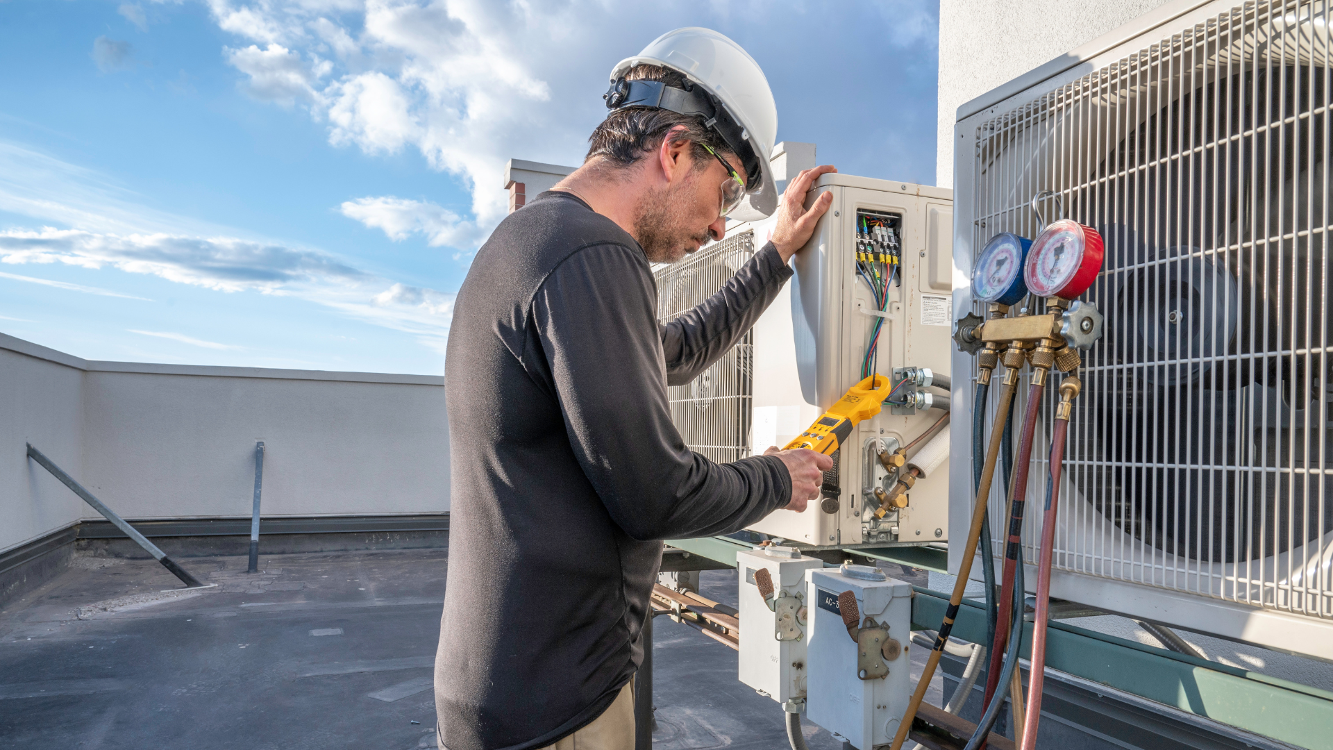 Technician checking HVAC gauges on a rooftop unit under a blue sky