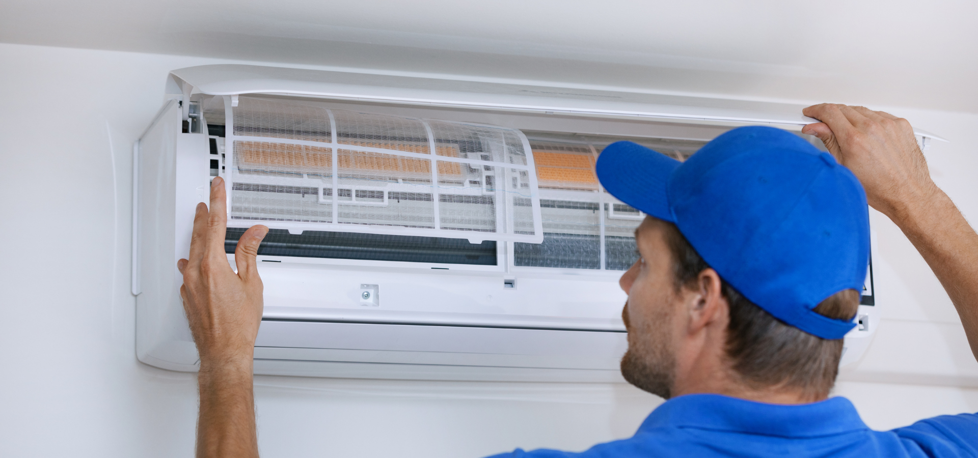 Technician installing a white air conditioner unit on a wall under a ceiling