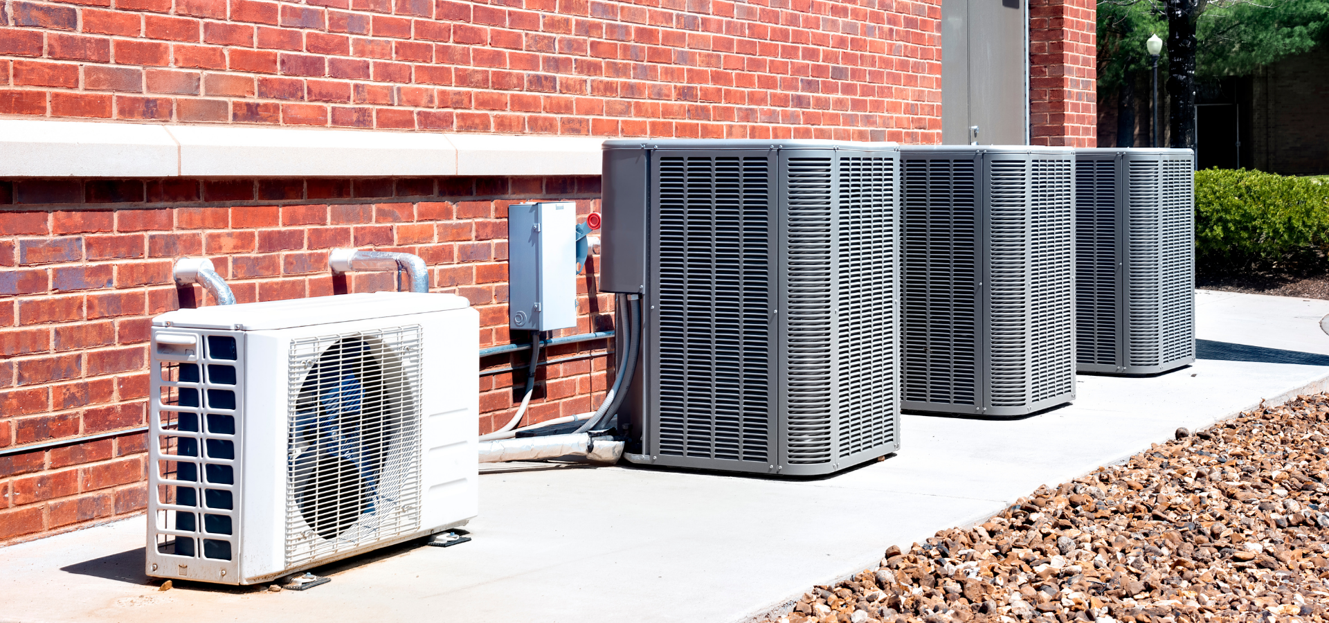 Outdoor air conditioner units beside a brick building on a paved foundation