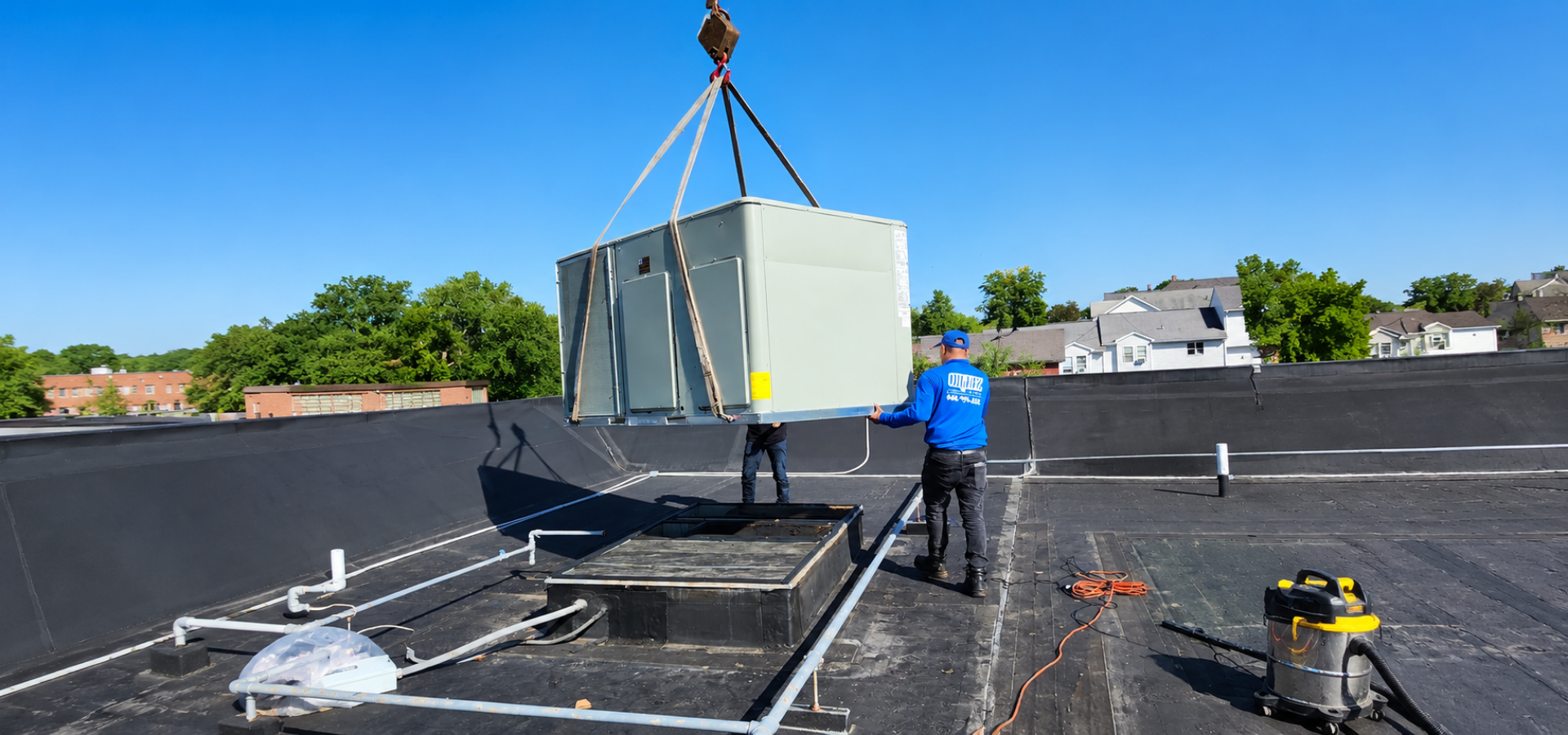 Worker on a rooftop using a crane to lift a large HVAC unit into place.