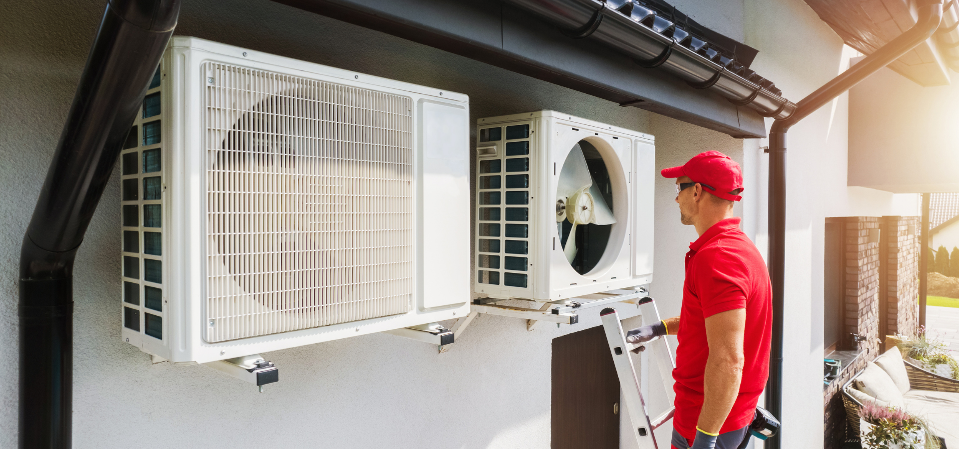 Technician in red uniform inspecting outdoor air-conditioning units on a house wall