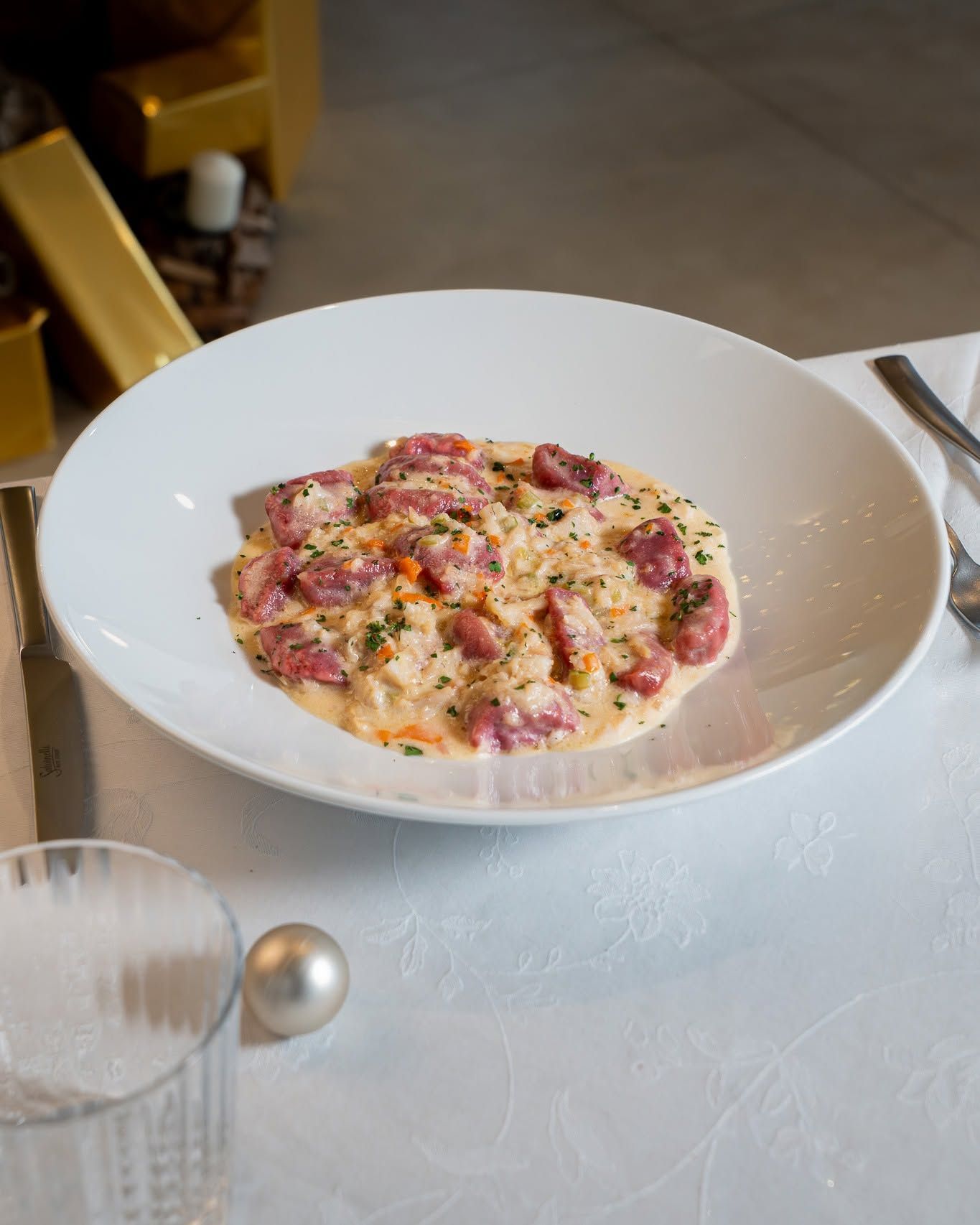 Pasta o risotto rosa cremoso in una ciotola bianca su una tovaglia, con le posate accanto.