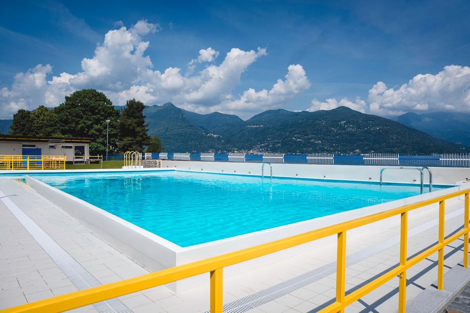 Piscina all'aperto con ringhiera giallo brillante e vista sulle montagne sotto un cielo azzurro nuvoloso.