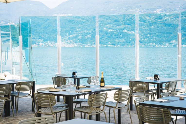 Tavolini e sedie da caffè all'aperto in riva a un lago blu con le montagne sullo sfondo.