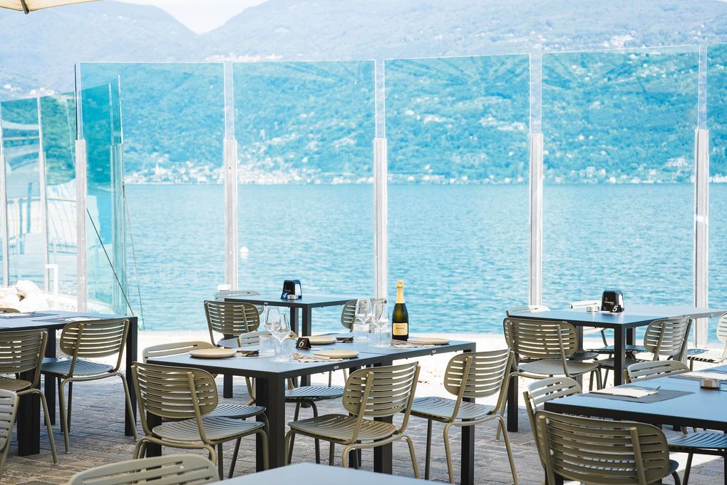 Tavolini e sedie da caffè all'aperto in riva a un lago di un blu intenso, con le montagne sullo sfondo.