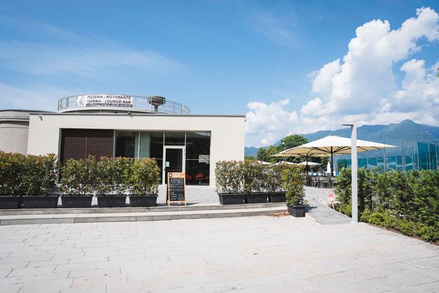Caffetteria moderna con tavolini all'aperto e vista sulle montagne sotto un cielo azzurro brillante.