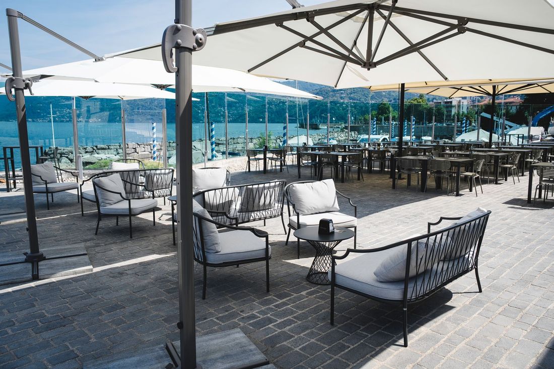 Terrazza esterna del caffè con tavoli, sedie e ombrelloni color crema neri, affacciata sull'acqua.