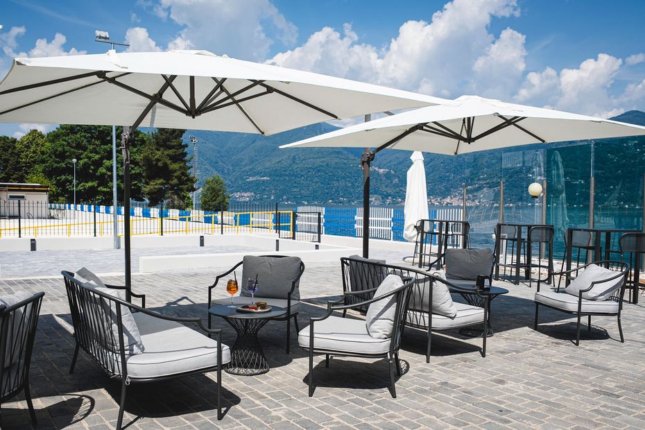 Patio esterno con sedie nere, ombrelloni bianchi e vista sulle montagne in riva al mare.