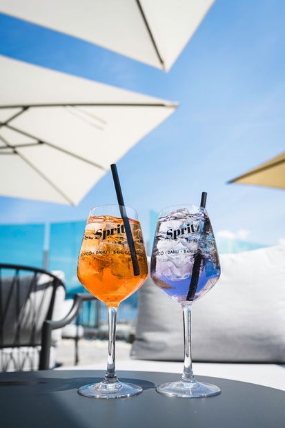Due cocktail colorati con cannucce su un tavolo da patio all'aperto sotto ombrelloni bianchi