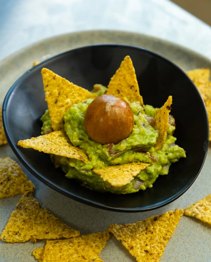 Ciotola nera di guacamole con tortilla chips e guarnizione di pomodorini ciliegino su un piatto