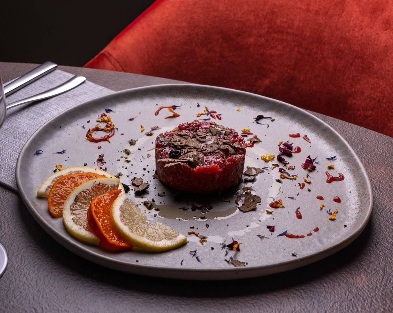 Medaglione di bistecca impiattato con fette d'arancia e guarnizione su un piatto grigio.