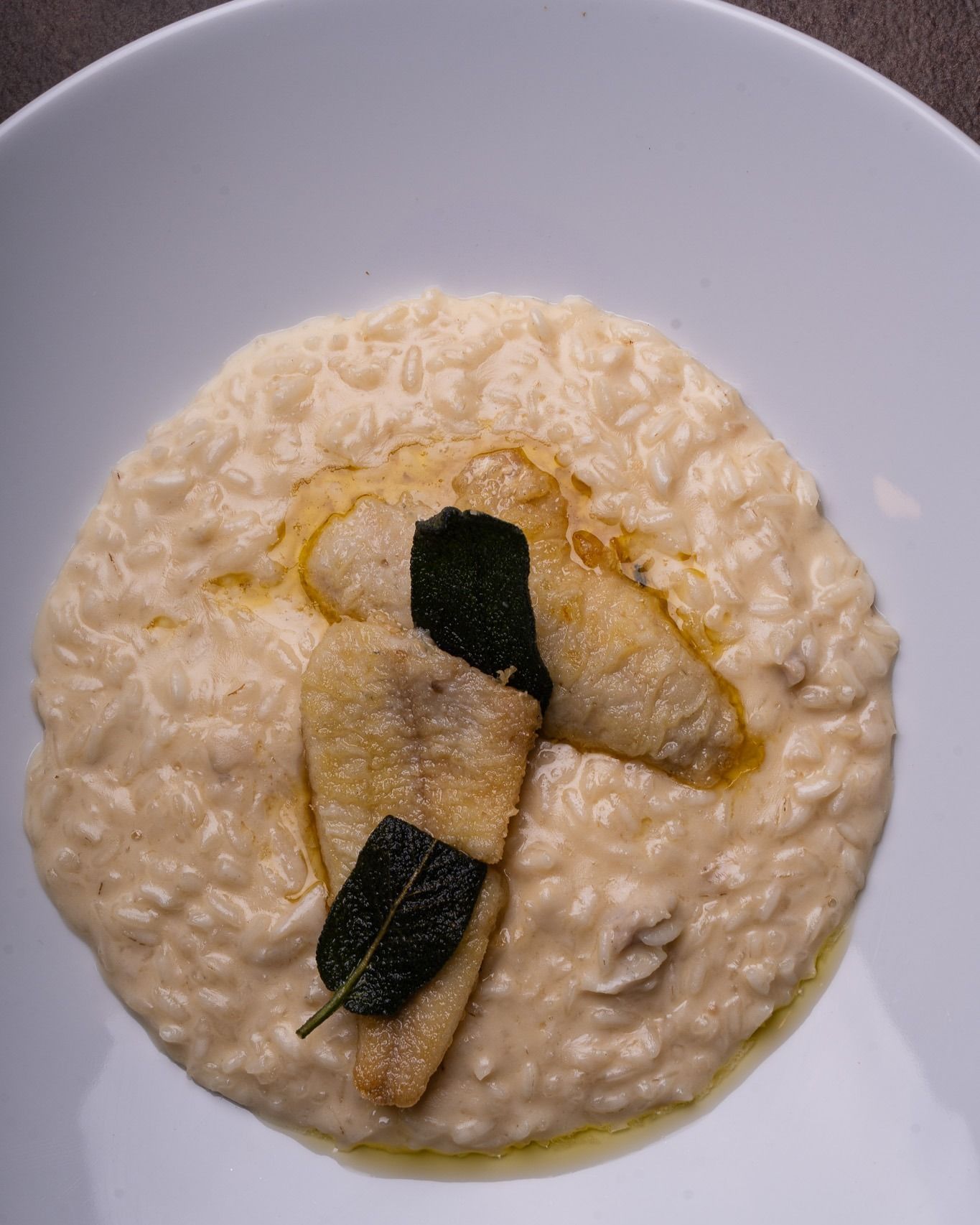 Risotto cremoso su un piatto bianco, guarnito con due capesante scottate ed erbe aromatiche verde scuro.