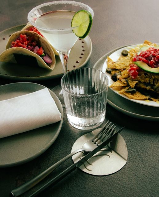 Un pasto a base di tacos su un tavolo con una bevanda, un bicchiere vuoto e posate su piatti verde scuro.